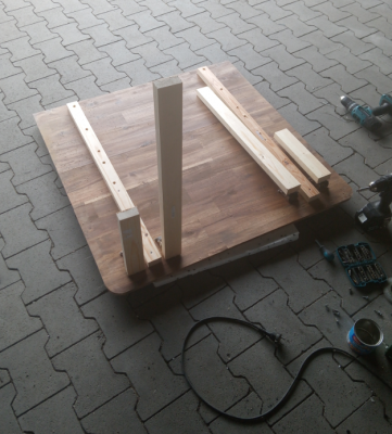Tischplatte von unten: Zur verstärkung der &quot;nur&quot; 2cm dicken Platten (die Tischplatte wurde aus drei Teilen zusammengesetzt) wurden zwei Kanthölzer verklebt und geschraubt.<br />Vorne sieht man die zwei Paar Tischbeine, in der Mitte die Langen um den Tisch als Tisch benutzen zu können, außen die kurzen um den Tisch weiter unten als Liegefläche zu verwenden.<br />Die Bolzen an der Rückseite fehlen auf dem Foto noch