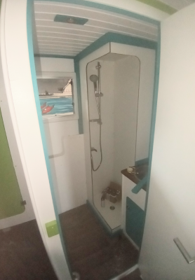 Die Duschkabine wurde im vorderen Bereich des Badezimmers zusammengebaut und anschließend an ihre jetzige Position geschoben. Befestigt wurde sie mit Klebmasse an den Wänden und über die blauen Umrandungshölzer am Boden und an der Decke.