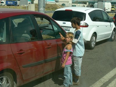 Schlimm! an der Serbisch- Ungarischen Grenze zum Betteln losgeschickte Romakinder. <br />Es gibt bei näherer Betrachtung eine Hirarchie: zwei ältere Jungs, die den Kleinen, die überall herumwuseln, Kommandos zurufen und erbetteltes Geld einziehen. <br />Blitzartig wird der Angebettelte gewechselt, wenn ein anderes, lukrativer aussehendes Fahrzeug naht.<br /> Dem Jüngsten fehlte die rechte Hand- dass er sie beim Spielen eingebüßt hat, oder ob sie ihm, um Aufmerksamkeit zu erheischen, abgehackt wurde? <br />Wir sahen auch mehrere junge Romi mit dem &quot;immer schlafenden Kind&quot; auf dem Arm. Fährt man ins Hinterland, sieht man die Paläste, <br />die sich die Romafamilien bauen. Übrigens nicht nur in Serbien. In Rumänien und der Ukraine sahen wir<br /> die gleichen goldglänzenden Dächer, Türmchen, gotischen Fenster wie sie die Zigeunerbarone so gern haben.<br />.
