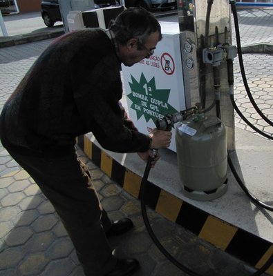 Der portugisiesche Tankwart füllt 24 Liter Gas zum Preis von 18 Euro in die grau-deutsche 11-KG-Flasche.
