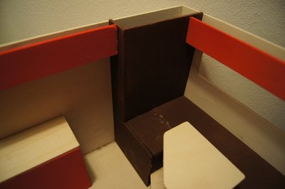 Hinten in Fahrtrichtung rechts:<br />An die U-Sitzgruppe ist ein breiter Schrank, in den alle Elektrik reinkommt und Fächer für Glaser/Teller. In die Bank links kommen die 4 Batterien auf Teleskopschienen (ca 600 bis 800 Ah), die von außen zu wechseln sind. Neben dem Schrank kommt die Eingangstür. Hier ist noch unklar, ob wir eine Stufe in den Aufbau reinbauen oder die Unterkante Tür auch Höhe Boden ist. Im zweiten Fall (ohne Stufe) bekommt sie eine ausziehbare Leiter, die in den Zwischenrahmen oder (s. weiter unten) in den Zwischenboden reingeschoben wird.